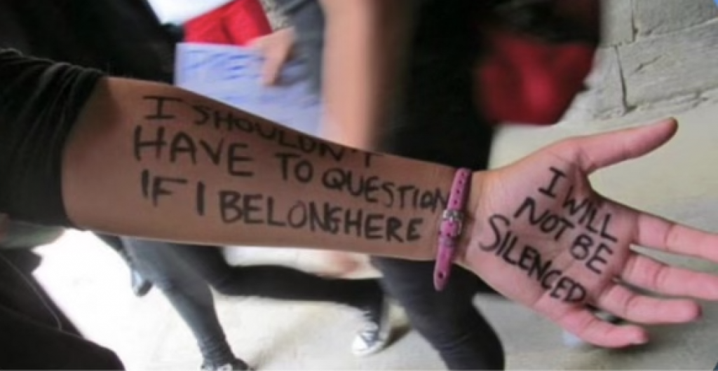Photo of hand with the following writing "I shouldn't have to question if I belong here" "I will not be silenced"